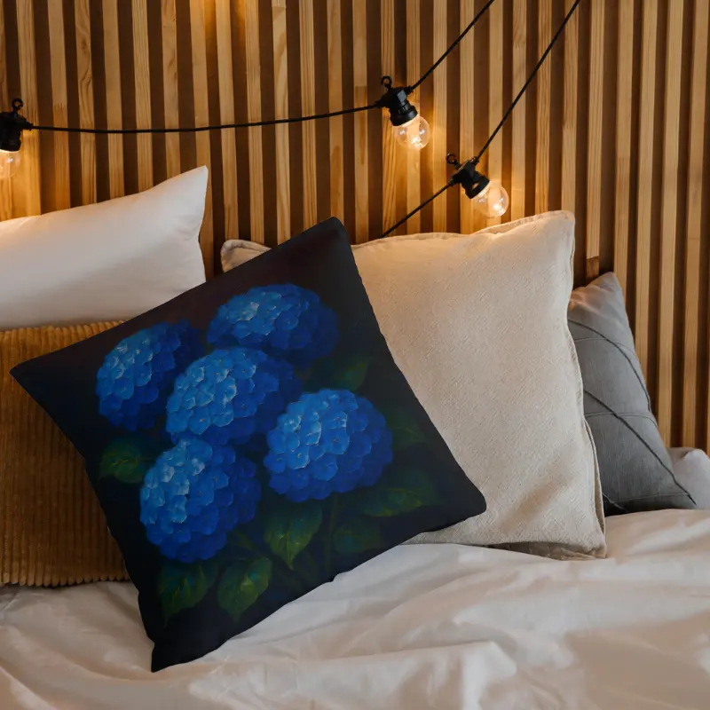 Blue hydrangea oil-impasto throw pillow on light bedding with charcoal background tones and textured green leaves