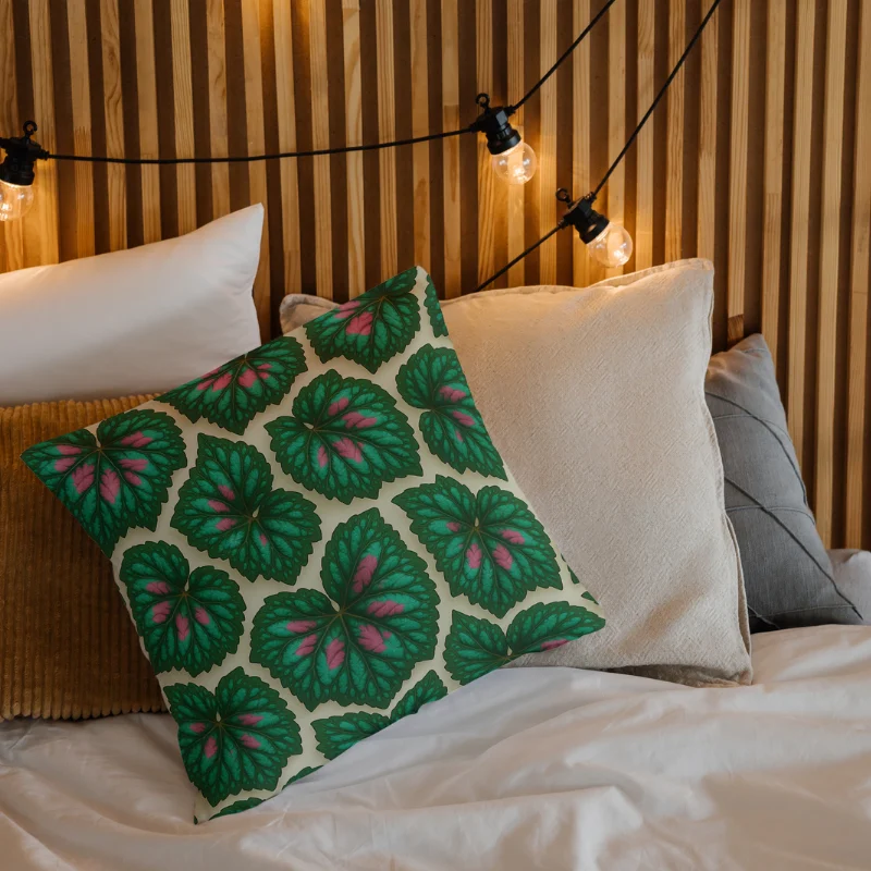 Begonia Rex floral throw pillow with glossy green and pink leaves on a cozy bed