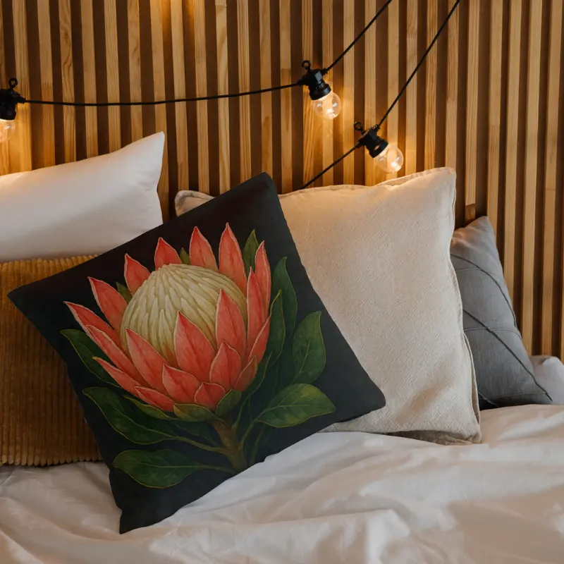 Watercolor King Protea pillow showcasing coral blush petals, ivory center, and bold green leaves on charcoal.